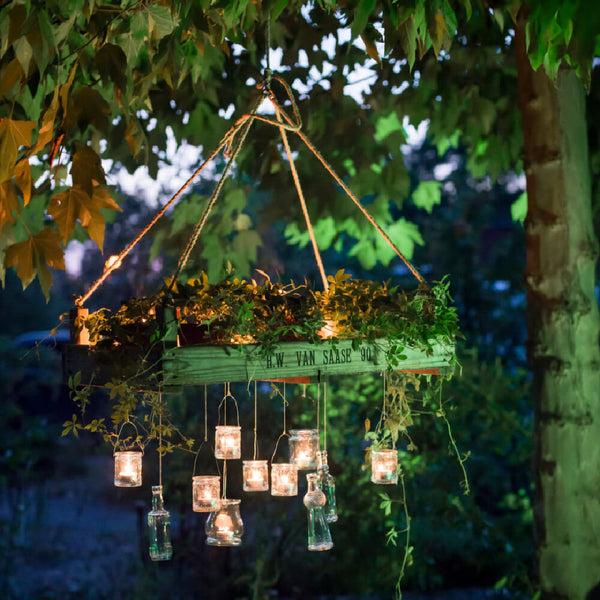 Panier de fleurs suspendu avec des plantes et des bougies dans des verres illuminés par la lumière du soir