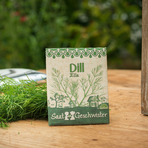 Sachet de graines d'aneth étiqueté « Ella » par Saat-Geschwister sur une table en bois avec de l'aneth frais en arrière-plan.