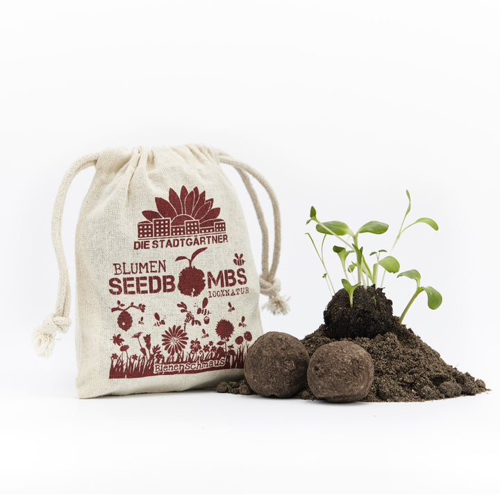 Sac en jute avec l'impression « Die Stadtgärtner Blumen Seedbomben », à côté de semis et de boules de terre sur fond blanc
