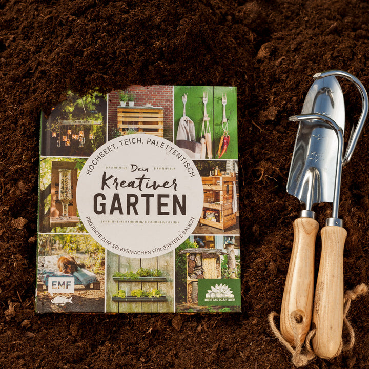 Livre de jardinage intitulé « Votre jardin créatif » sur le sol à côté d'outils de jardinage.