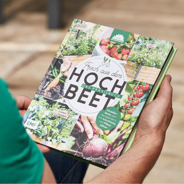 Personne tenant un livre de jardinage intitulé « Fraîchement sorti du lit surélevé » avec diverses images de jardinage et de récolte.