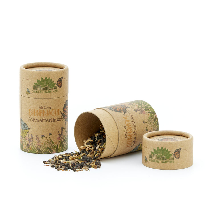 Mélange de graines pour abeilles et papillons dans deux tubes en carton avec l'inscription « Aktion BIENENWOHL Schmetterlinge » et le contenu renversé à côté d'un tube renversé.