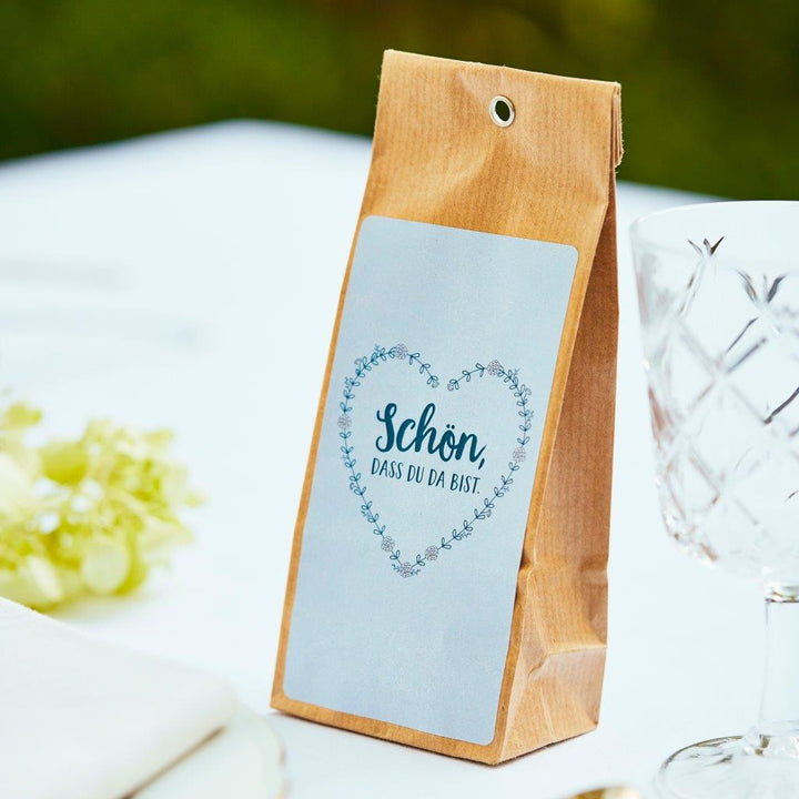 Sac en papier brun avec l'inscription « Ravi de vous avoir ici » sur une table à côté d'un verre à vin et de raisins.