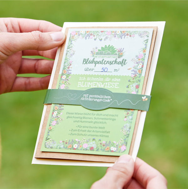 Mains tenant une carte-cadeau pour un pétale de fleur de plus de 50 mètres carrés avec un motif floral et du texte dessus.