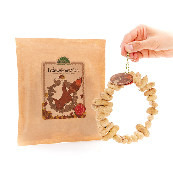 Main tenant un collier d'arachides pour écureuils à côté d'un sac étiqueté « Couronnes d'arachides ».