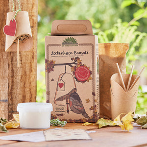 Emballage d'un kit de friandises pour oiseaux avec cloche d'alimentation et décoration naturelle en arrière-plan.