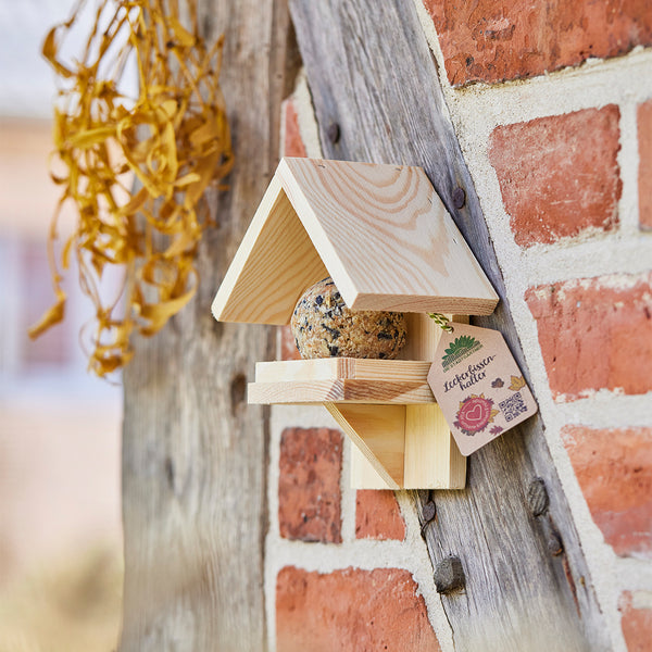 Nichoir en bois avec boules de suif fixées à un mur de briques.
