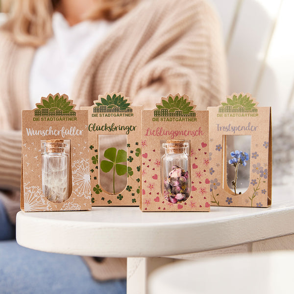 Quatre petits cadeaux des « jardiniers de la ville » sur une table, avec des étiquettes telles que « Remplisseur de souhait », « Porte-bonheur », « Personne préférée » et « Doudou ».